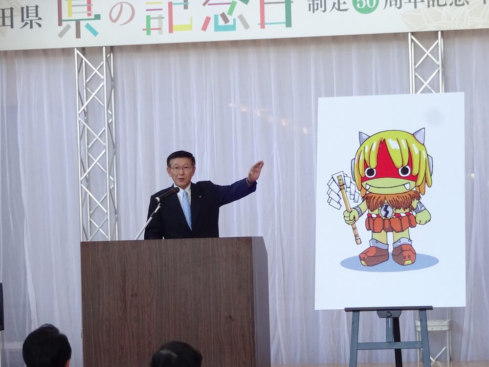 写真：ステージ上のボードに描かれた秋田県PRキャラクターを示す知事