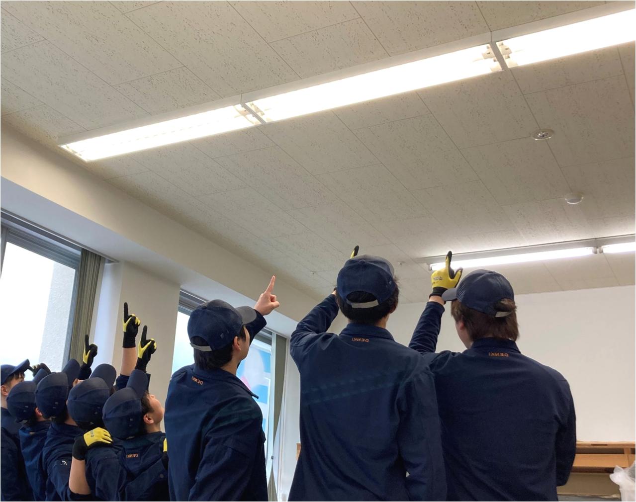 電気のトレーニーが照明を指さしている